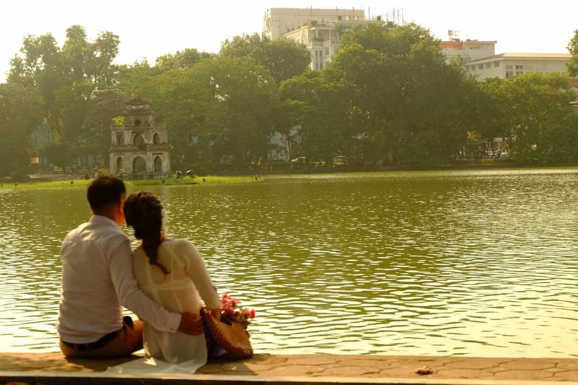 Un couple assis au bord du lac Hoan Kiem à Hanoï lors d'un voyage personnalisé au Vietnam, admirant la célèbre Tour de la Tortue.