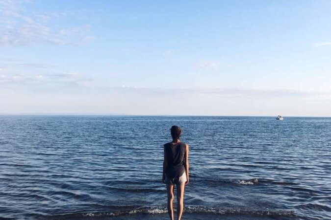 Une personne debout face à l'immensité de l'océan pour profiter du bord de mer en toute sérénité.