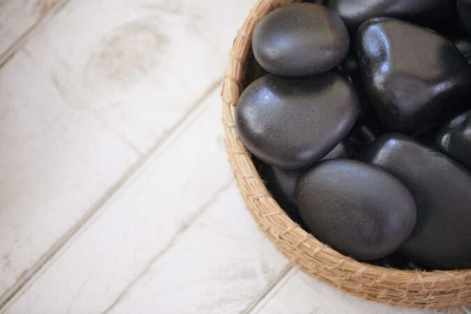 Pierres noires lisses disposées dans un petit panier en osier pour un massage aux pierres chaudes relaxant.