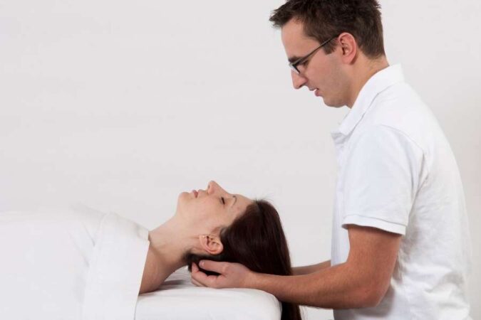 Un praticien en tenue blanche masse le crâne et la nuque d'une femme allongée lors d'une séance de massage crânien shirotchampi.