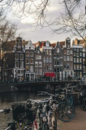 Vélos hollandais garés le long d'un canal calme à Amsterdam, avec les maisons de ville historiques en arrière-plan sous un ciel nuageux, une scène parfaite pour découvrir Amsterdam autrement.