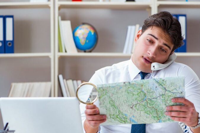 Un agent de voyage indépendant étudie une carte géographique avec une loupe tout en répondant au téléphone.
